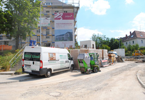 Reinigungsfahrzeuge und Personal bei der Straßen- und Gehwegreinigung vor einem Neubau.