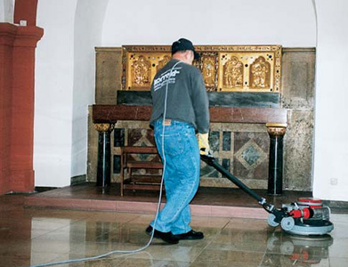Person säubert mit einer Maschine den Boden in einem Kirchenschiff.