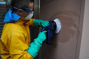 Reinigungskraft in gelber Schutzkleidung schrubbt eine verschmutzte Wand mit Maschine.