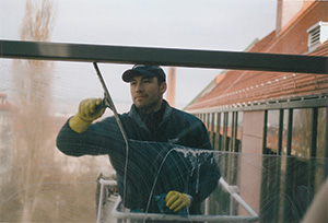 Reinigungskraft säubert ein Fenster von außen mit Handschuhen und Abzieher.