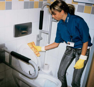 Korrekt Reinigungskraft säubert WC mit gelben Gummihandschuhen und Schwamm.