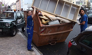 Zwei Personen werfen Sperrmüll in einen offenen Container auf der Straße.