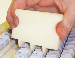 Hand reinigt eine Computertastatur mit einem speziellen Schwammaufsatz.
